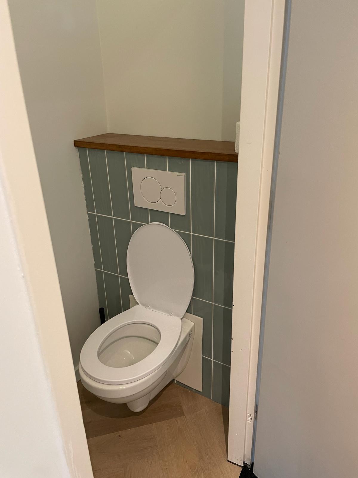 Toilet met groen verticaal tegelwerk en houten plank